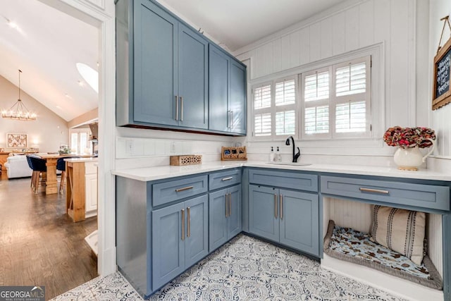 kitchen featuring a sink, an inviting chandelier, light countertops, blue cabinetry, and lofted ceiling