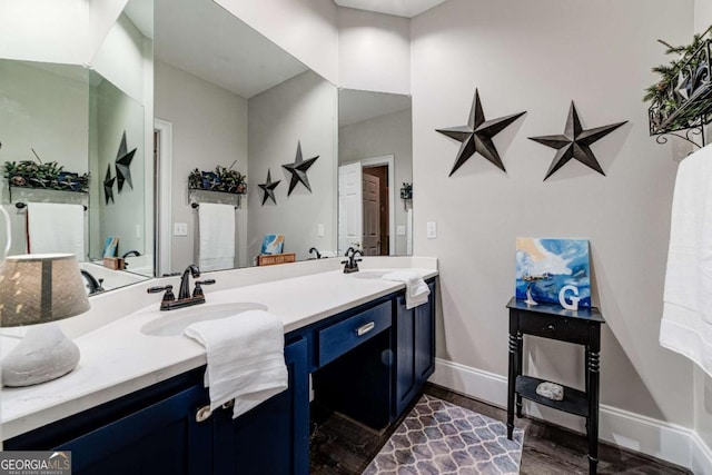 bathroom with double vanity, wood finished floors, a sink, and baseboards