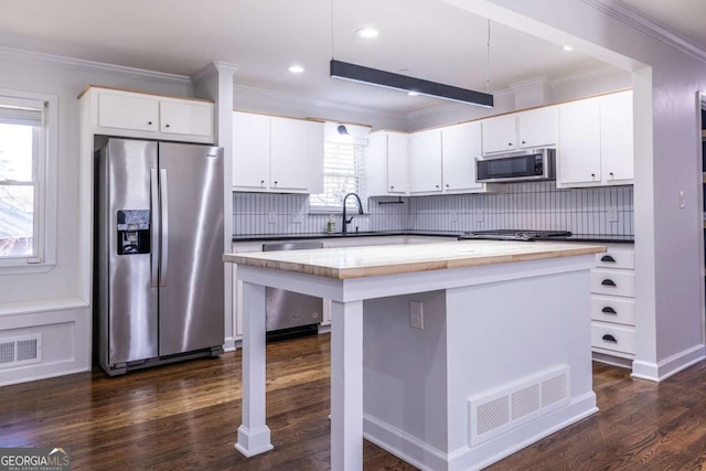 kitchen with dark wood-style floors, visible vents, stainless steel appliances, and ornamental molding