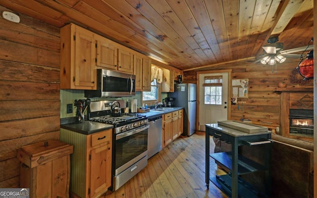 kitchen with a glass covered fireplace, dark countertops, stainless steel appliances, light wood-style floors, and a sink