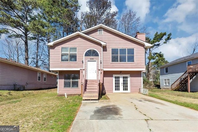 raised ranch featuring a front yard, a chimney, concrete driveway, and french doors