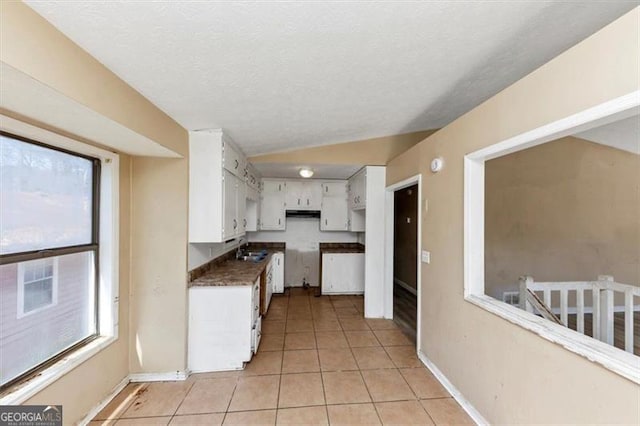 kitchen with lofted ceiling, light tile patterned flooring, white cabinets, and a healthy amount of sunlight