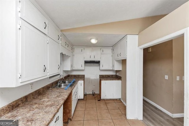 kitchen with light tile patterned floors, baseboards, lofted ceiling, white cabinetry, and a sink