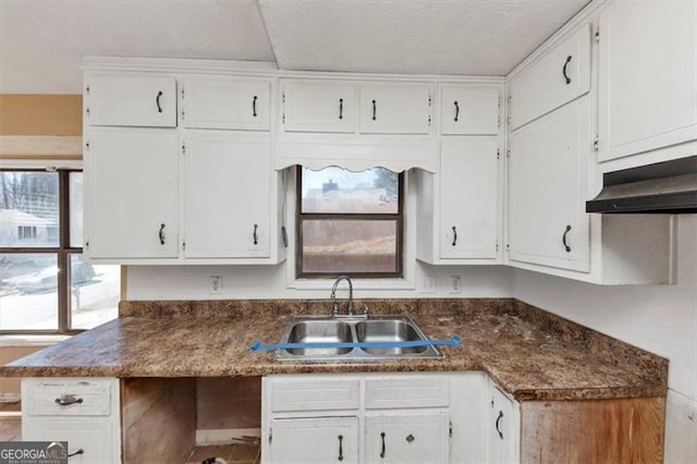 kitchen featuring dark countertops, a sink, white cabinetry, and under cabinet range hood