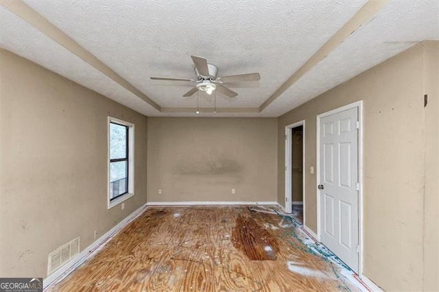 unfurnished room featuring baseboards, visible vents, a ceiling fan, a raised ceiling, and a textured ceiling