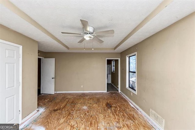 unfurnished room featuring a tray ceiling, visible vents, a textured ceiling, wood finished floors, and baseboards