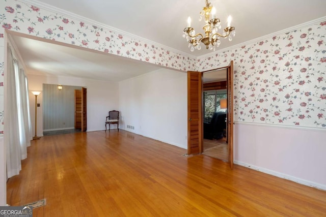 spare room with visible vents, ornamental molding, light wood finished floors, an inviting chandelier, and wallpapered walls