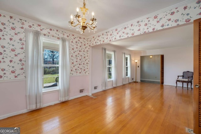 spare room featuring crown molding, light wood-style floors, wainscoting, and wallpapered walls