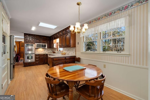 dining room featuring a skylight, wallpapered walls, baseboards, light wood-type flooring, and a notable chandelier