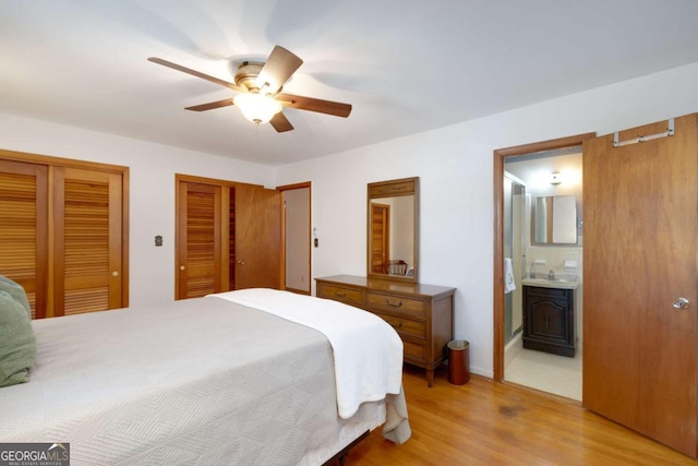 bedroom featuring multiple closets, light wood-style flooring, a wood stove, a sink, and ensuite bath