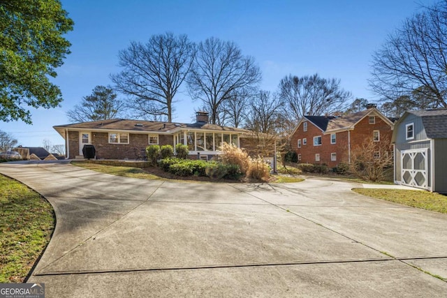 view of front facade featuring an outbuilding, brick siding, a chimney, a storage shed, and driveway