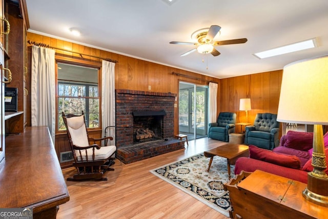 living area featuring wood walls, a skylight, a brick fireplace, light wood finished floors, and crown molding