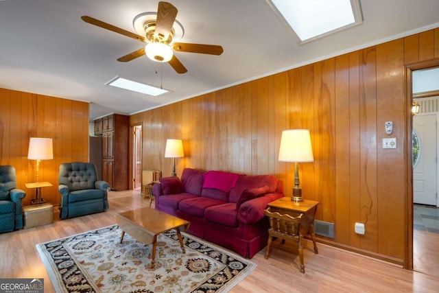 living area featuring a skylight, a ceiling fan, ornamental molding, and wood finished floors