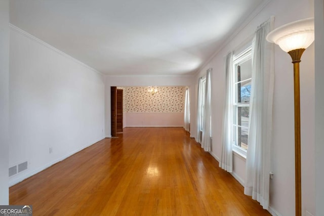 unfurnished room featuring light wood-style floors, baseboards, visible vents, and ornamental molding