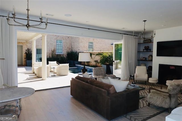 living area with a notable chandelier, a fireplace, wood finished floors, a healthy amount of sunlight, and decorative columns