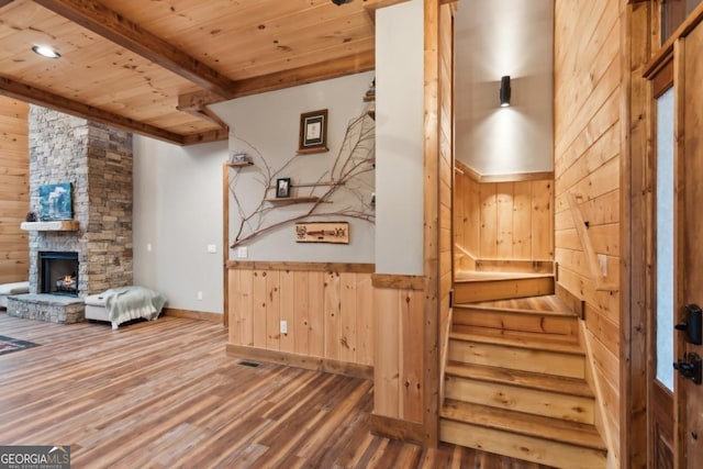 interior space with a stone fireplace, wooden walls, wood finished floors, wood ceiling, and beamed ceiling