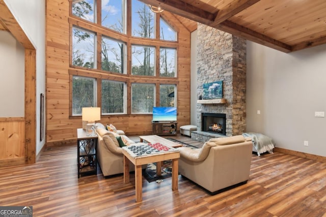 living room featuring wood ceiling, wood walls, a stone fireplace, wood finished floors, and beamed ceiling