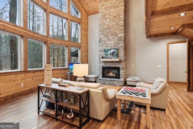 living area featuring a fireplace, wood walls, wood finished floors, wooden ceiling, and beamed ceiling