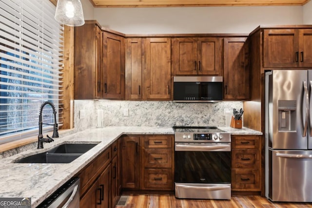 kitchen featuring appliances with stainless steel finishes, a sink, light stone counters, and decorative backsplash