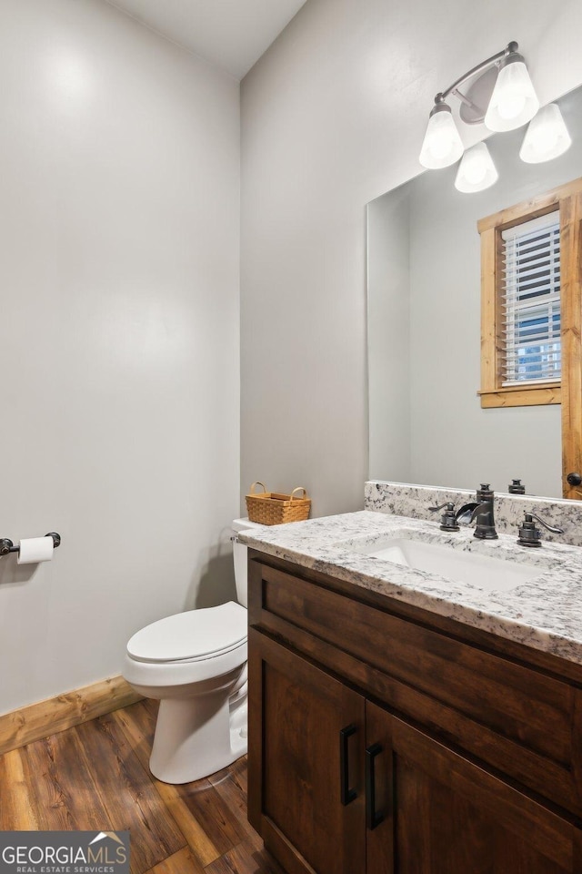 half bath featuring baseboards, vanity, toilet, and wood finished floors