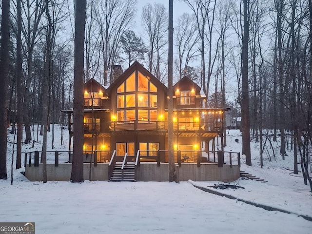 snow covered property with a balcony, a chimney, and stairway