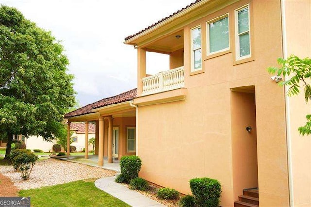 back of house featuring a tile roof, a balcony, and stucco siding