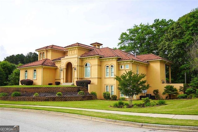 mediterranean / spanish home with stucco siding, a front lawn, and a tiled roof