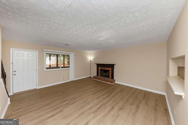 unfurnished living room with light wood-type flooring, a fireplace, a textured ceiling, and baseboards