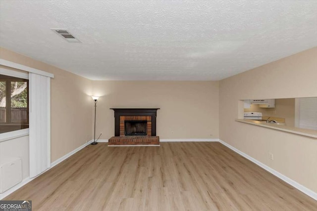 unfurnished living room with baseboards, visible vents, a fireplace, and light wood finished floors