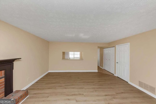 unfurnished living room featuring light wood-type flooring, baseboards, visible vents, and a textured ceiling