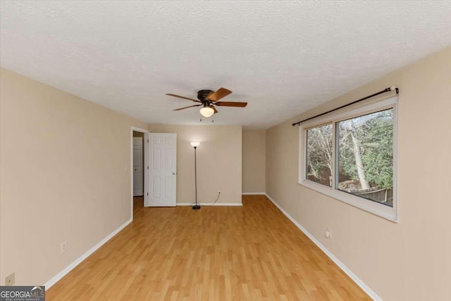 empty room with baseboards, a textured ceiling, and light wood finished floors