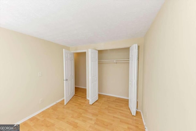 unfurnished bedroom featuring light wood-type flooring, a closet, a textured ceiling, and baseboards