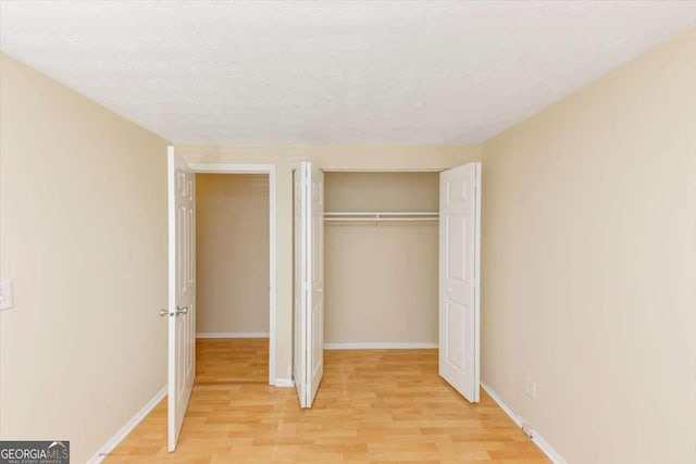 unfurnished bedroom with a closet, light wood-style flooring, baseboards, and a textured ceiling