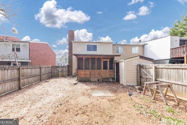 rear view of house featuring a sunroom, a fenced backyard, a chimney, and an outdoor structure