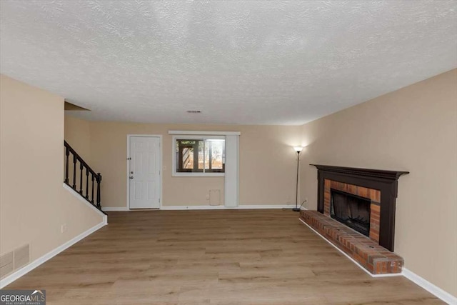 unfurnished living room with visible vents, stairway, light wood-style floors, a brick fireplace, and baseboards