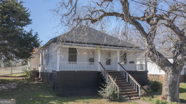 bungalow-style home with covered porch, roof with shingles, stairway, and fence