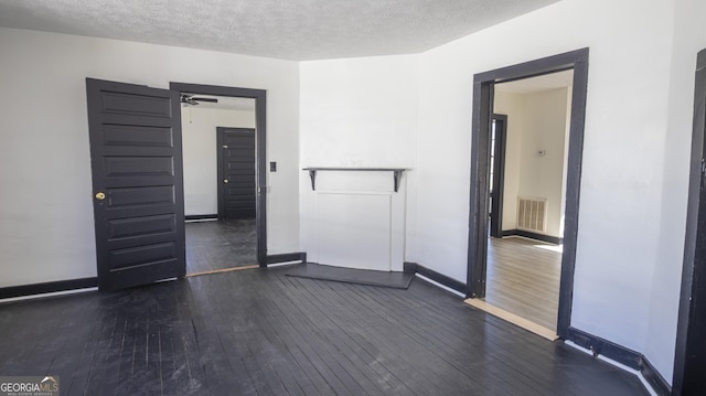 empty room featuring baseboards, visible vents, dark wood finished floors, and a textured ceiling