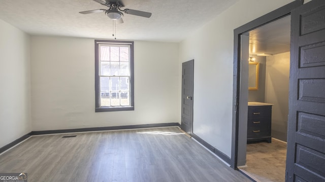 unfurnished bedroom featuring visible vents, a textured ceiling, baseboards, and wood finished floors