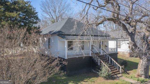 view of front of property featuring covered porch, roof with shingles, and stairway