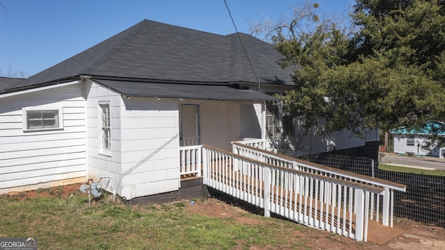 view of side of property with a shingled roof and fence