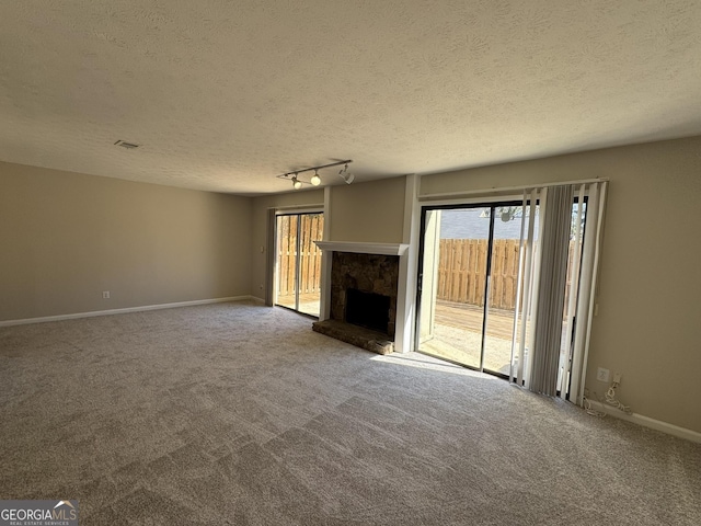 unfurnished living room with carpet flooring, a stone fireplace, track lighting, a textured ceiling, and baseboards