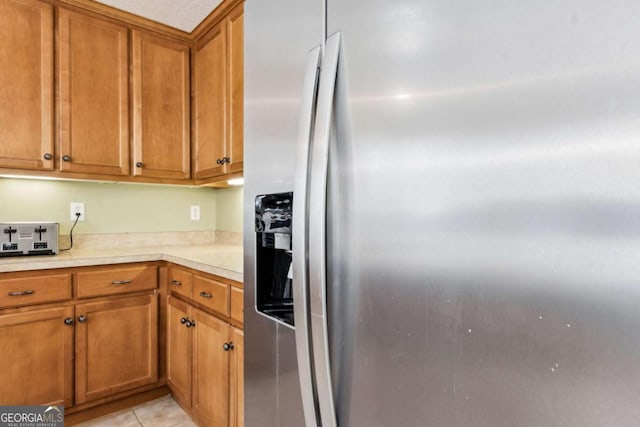 kitchen featuring light tile patterned floors, light countertops, brown cabinetry, and stainless steel fridge