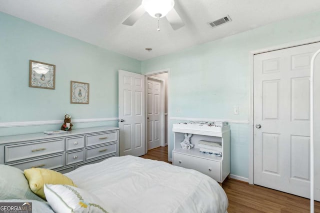 bedroom featuring a wainscoted wall, a ceiling fan, visible vents, and wood finished floors