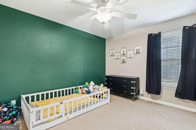 bedroom with carpet floors, a nursery area, ceiling fan, and baseboards