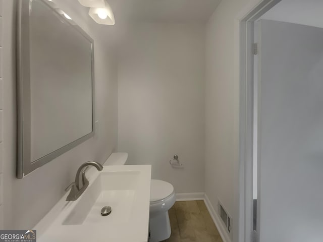 half bathroom with visible vents, vanity, toilet, and baseboards