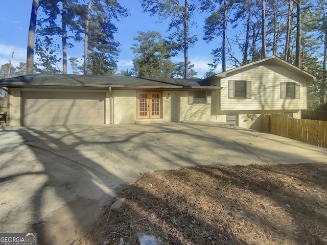 view of property exterior with a garage, brick siding, fence, concrete driveway, and french doors