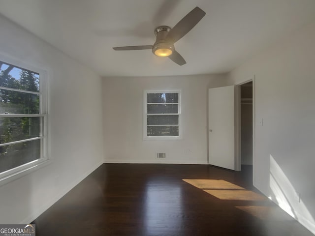 empty room with visible vents, wood finished floors, a ceiling fan, and baseboards