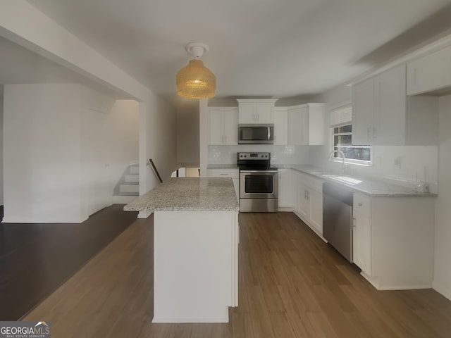 kitchen with stainless steel appliances, dark wood-type flooring, white cabinetry, light stone countertops, and tasteful backsplash