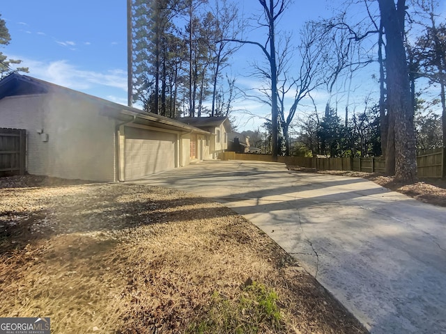 exterior space featuring a garage, concrete driveway, and fence