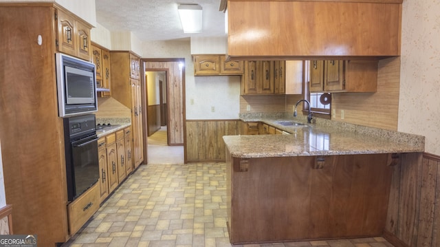 kitchen featuring stainless steel microwave, wainscoting, a sink, oven, and wallpapered walls